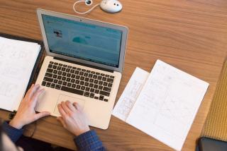 Ordinateur portable ouvert sur un bureau clair, la main de son utilisateur posée près du clavier